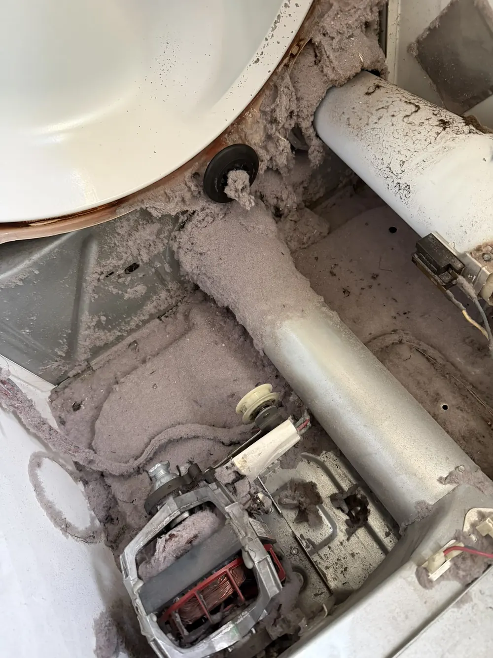 Heavy lint and dust buildup inside dryer cabinet around motor and duct