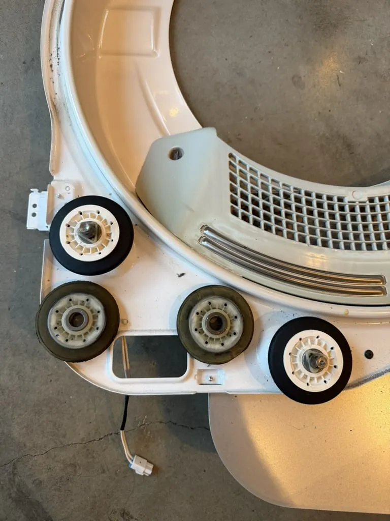 New dryer drum rollers beside worn rollers during replacement
